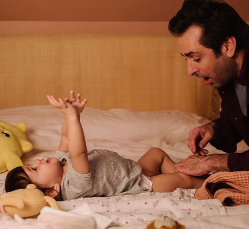 Papa surpris qui change la couche de son bébé qui est allongé sur le lit - Mustela Belgium - 1