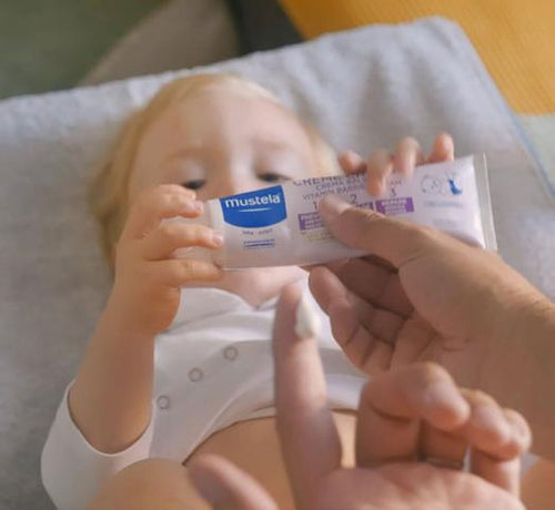 Bébé qui tient dans ses mains la crème change Mustela - Mustela Belgium - 1