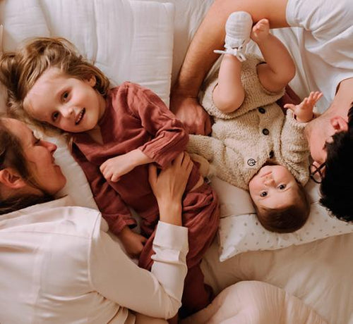 Deux parents allongés sur un lit avec leurs deux filles - Mustela Belgium - 1