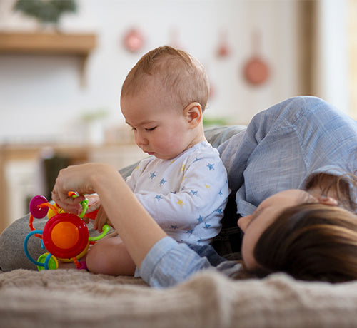 Maman allongée sur un lit qui joue avec son bébé - Mustela Belgium - 1