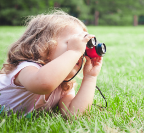 Enfant fille dans l'herbe jouant avec des jumelles - Mustela Belgium - 1