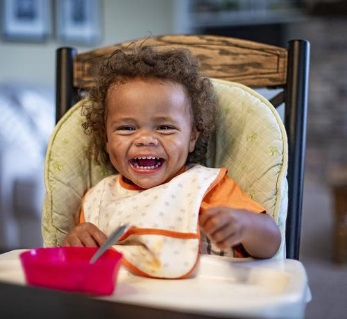 Enfant assis sur une chaise haute qui rigole - Mustela Belgium - 1