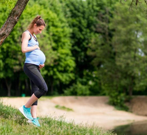 Femme enceinte en tenue de sport regardant son ventre dans un parc  - Mustela Belgium - 1