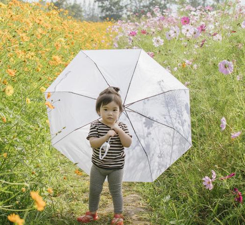 Enfant debout dans un champs de fleurs portant un parapluie - Mustela Belgium - 1