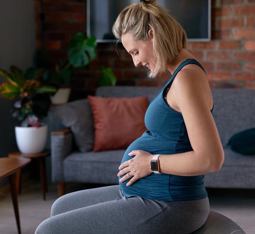 Femme blonde enceinte qui est assise sur un ballon et qui se regarde le ventre