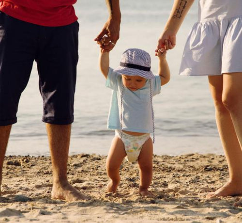 Bébé marchant sur la plage grâce aux mains de ses parents - Mustela Belgium - 1