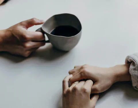 Une main tient une tasse de café pendant qu'une autre main se tend avec inquiétude, exprimant un besoin de soutien et d’écoute. - Mustela Belgium - 1