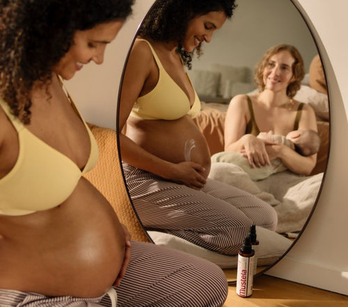 Une femme enceinte qui s'applique de la crème vergetures sur le ventre et une femme avec un bébé qui se regarde dans le mirroir - Mustela Belgium - 4