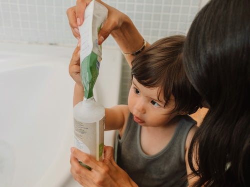 Une maman remplissant le flacon Mustela Famille Gel Lavant Bio Recharge 400ml avec l'aide de son petit garçon dans une salle de bain - Mustela Belgium - 2
