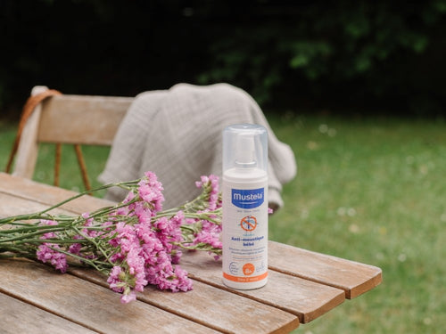 Le Lait Anti-Moustique Bébé et Famille Mustela est posé sur une table de jardin à côté de fleurs roses - Mustela Belgium - 6