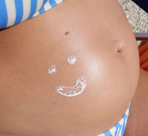 photo du ventre arrondi d’une femme enceinte, décoré d’un smiley dessiné avec de la crème solaire - Mustela Belgium - 1