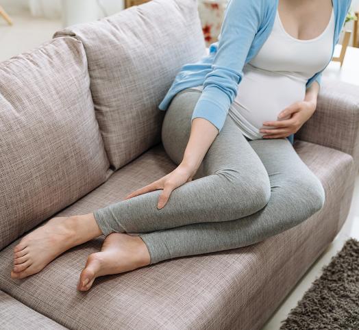 Femme enceinte en legging gris assise sur un canapé beige