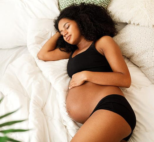 Femme métisse enceinte allongée sur un lit qui dort - Mustela Belgium - 1