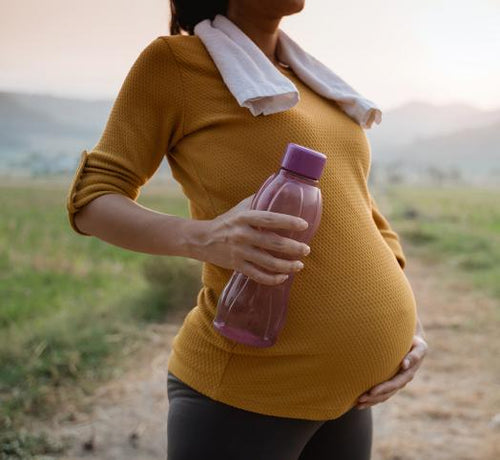 Femme enceinte qui se touche le ventre et qui porte une gourde rose dans sa main - Mustela Belgium - 1