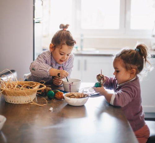Deux enfants filles assis à une table qui peignent des oeufs pour pâques - Mustela Belgium - 1