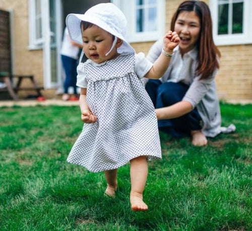 Enfant fille avec une robe et un chapeau blanc marchant dans l'herbe - Mustela Belgium - 1