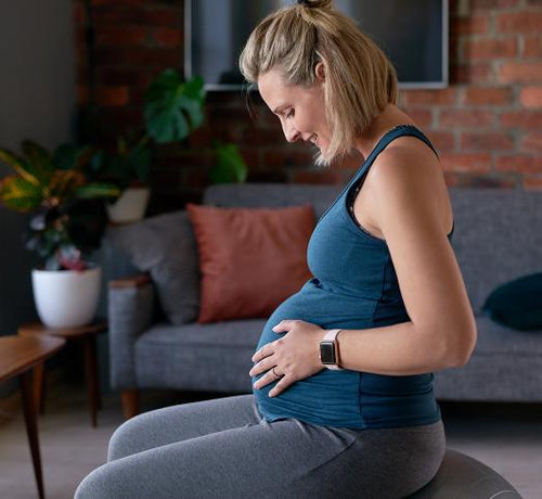 Femme blonde enceinte qui est assise sur un ballon et qui se regarde le ventre - Mustela Belgium - 1