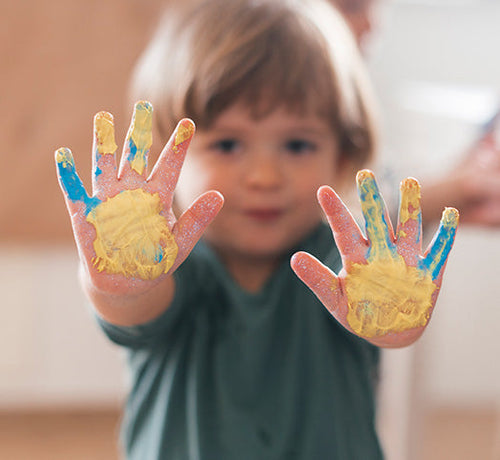 Visage enfant blond qui montre ses mains pleines de peinture - Mustela Belgium - 1