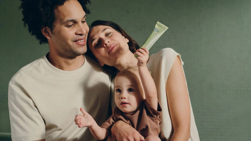 Une famille, composée d'une maman, d'un papa et d'un enfant au milieu tenu dans les bras de sa maman, avec à la main Mustela Famille Baume Universel Avocat Nourrissant - Mustela Belgium - 6