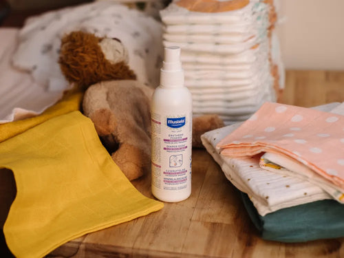 Spray change Mustela posé sur une table à côté des couches et des vêtements pour bébé - Mustela Belgium - 2